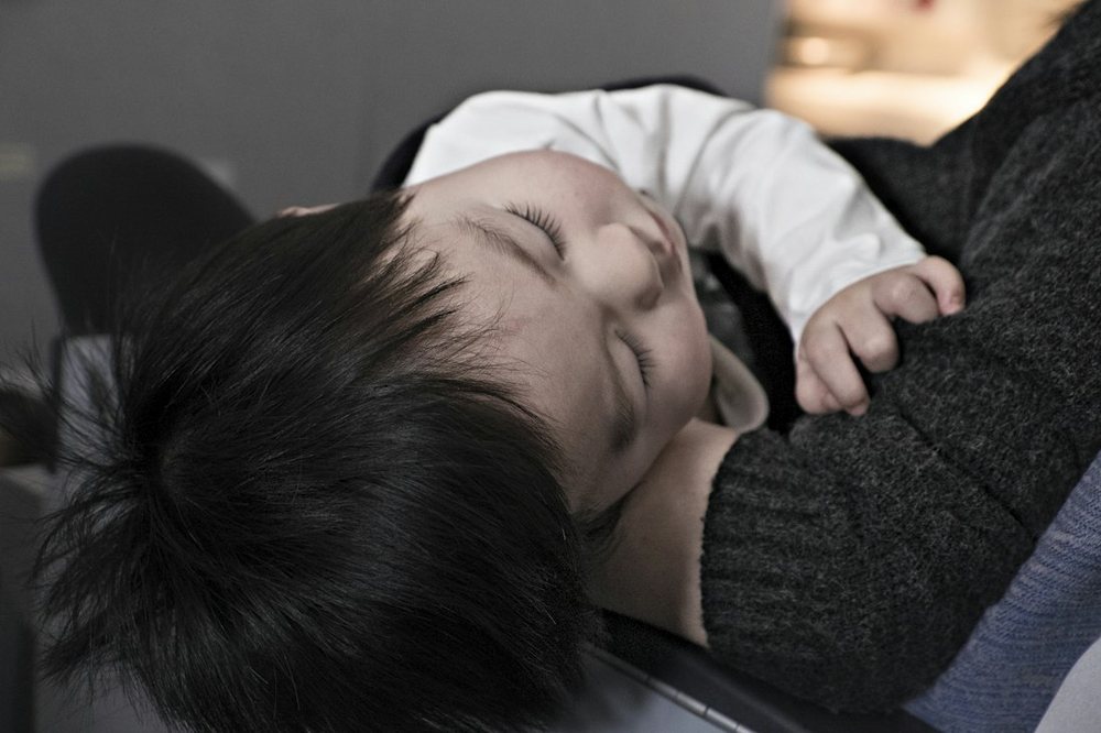 A toddler fast asleep on a parent's shoulder